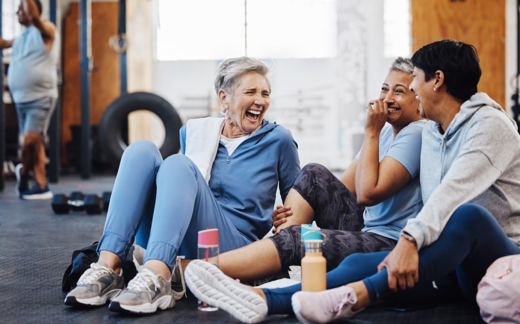 group of laughing mature woman taking a break at the gym for a story on fitness tips for seniors